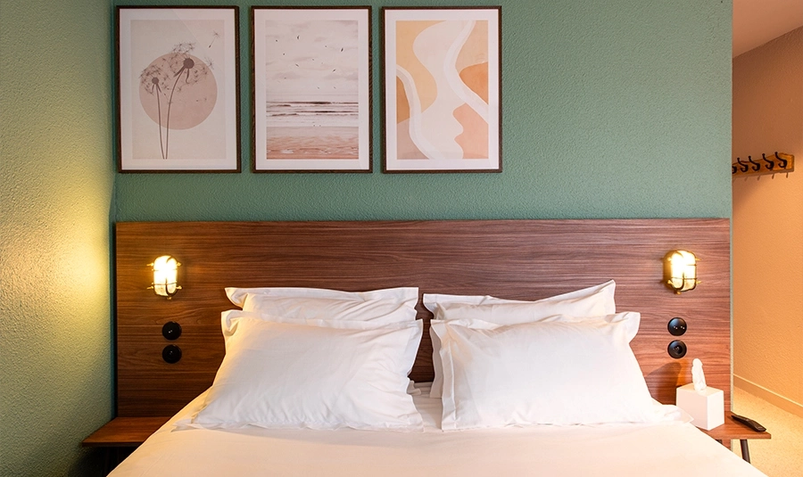 Holzkopfteil eines Standard-Doppelzimmers mit dekorativen Wandbildern und warmen Wandleuchten.