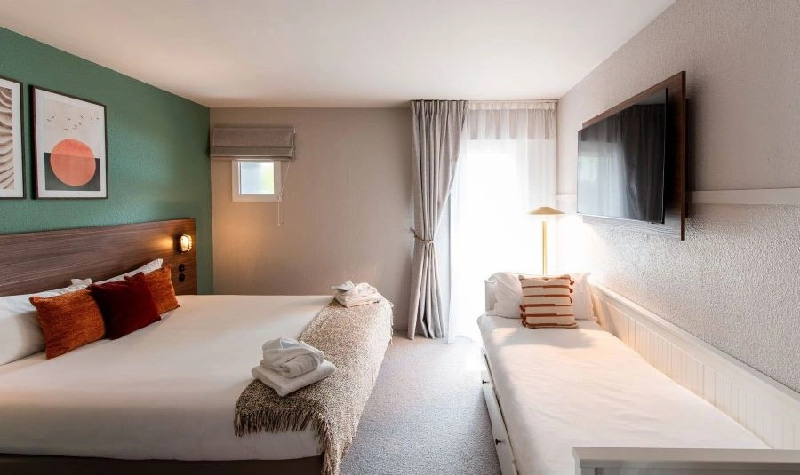 Dreibettzimmer mit Doppelbett, Schlafsofa, Wandfernseher und natürlichem Licht.