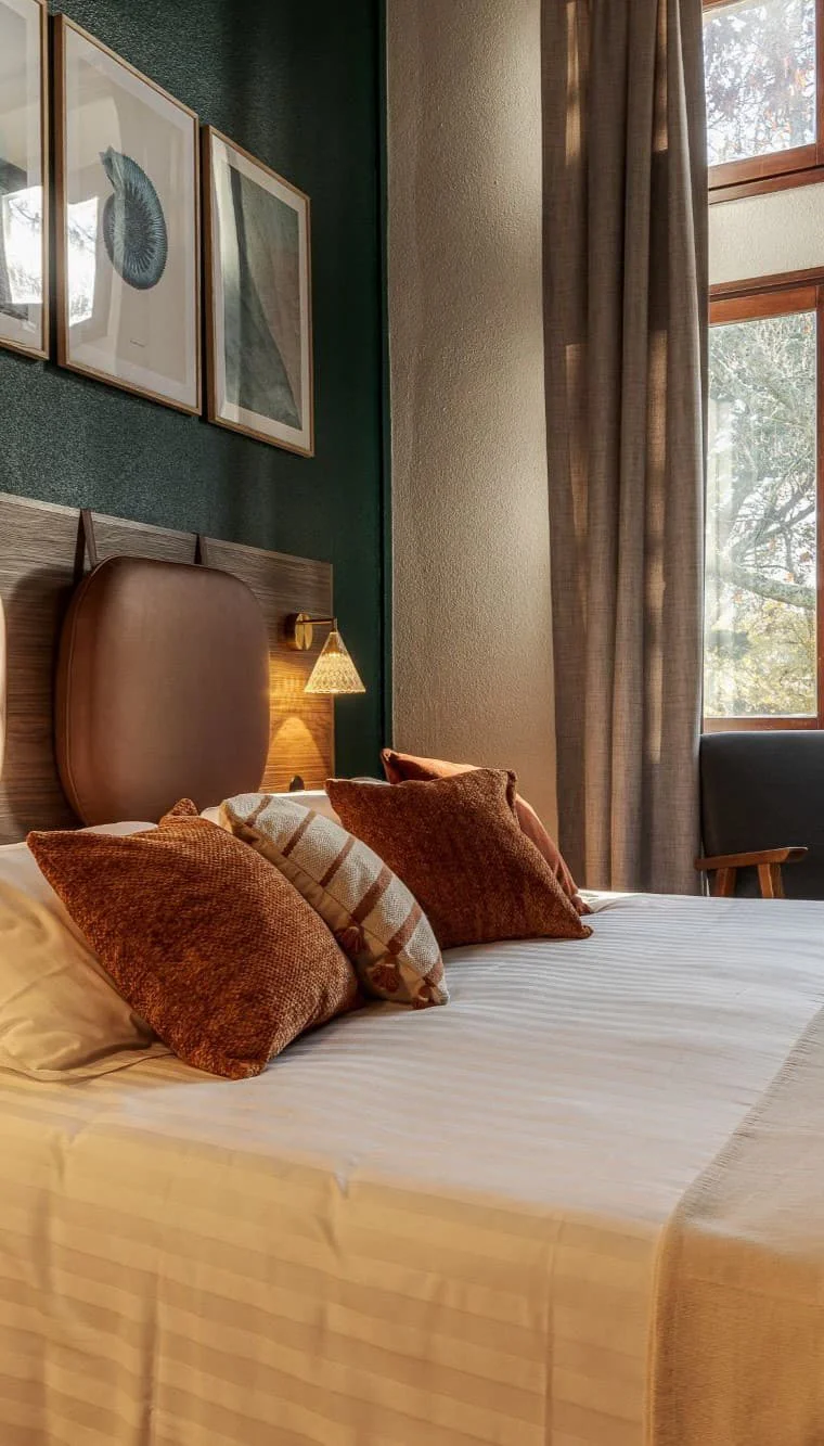 Chambre double du Manoir de la Maison OBONO : lit avec coussins terracotta, tête de lit en cuir, mur vert sapin, tableaux encadrés et fenêtre sur le parc