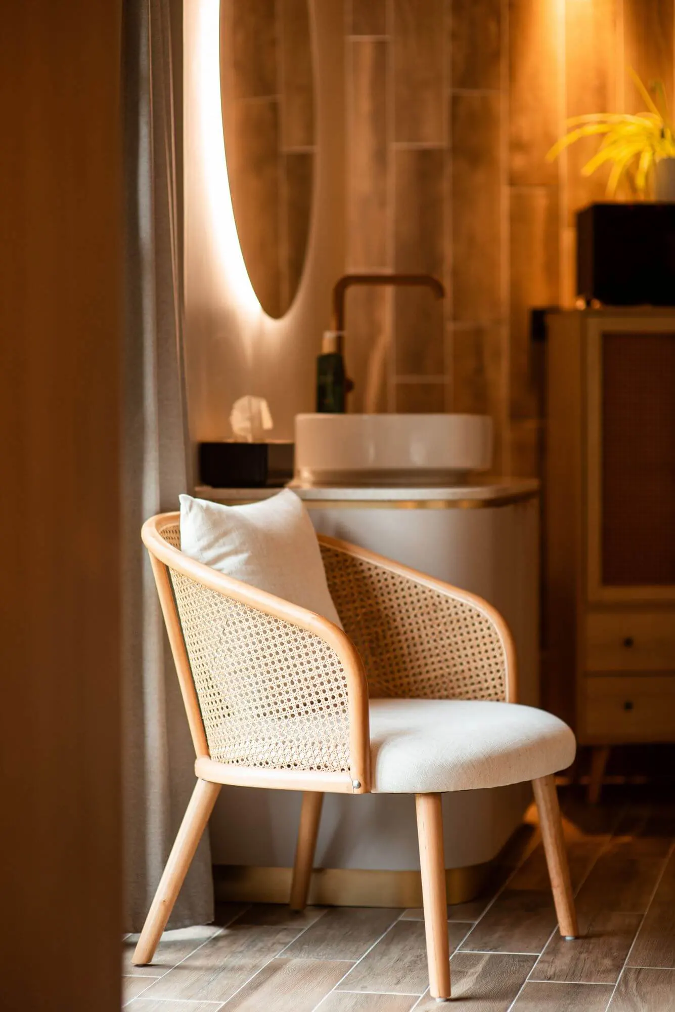 Fauteuil en rotin et salle de bain éclairée d'une chambre de la Maison OBONO, miroir rond rétroéclairé et vasque blanche