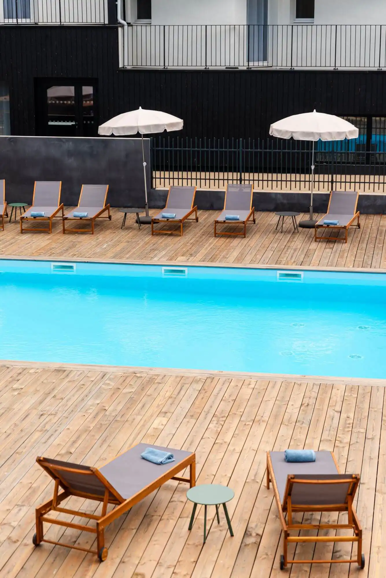 Piscine extérieure de la Maison OBONO avec transats en teck, parasols blancs et terrasse en bois