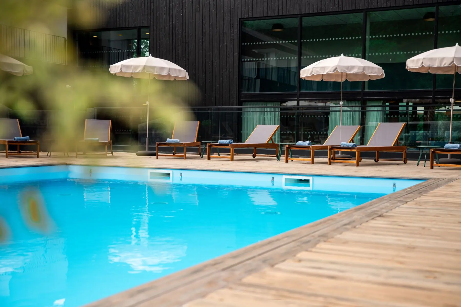 Piscine extérieure de La Maison Obono avec transats en bois et parasols blancs, terrasse en bois et façade noire vitrée